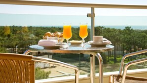 Un balcón con una mesa dispuesta para el desayuno, que incluye cruasanes, jugo y café, con vistas a un paisaje hermoso.