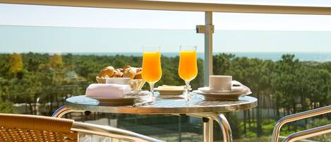 Un balcón con una mesa dispuesta para el desayuno, que incluye cruasanes, jugo y café, con vistas a un paisaje hermoso.
