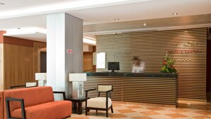 Zona de recepción de un hotel con diseño moderno, que incluye un mostrador de recepción, un sofá, una silla y una alfombra roja.