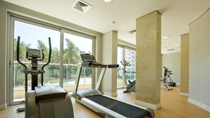 Un gimnasio con cintas de correr, elípticas y bicicletas estáticas, amplias ventanas y vistas a árboles y edificios.