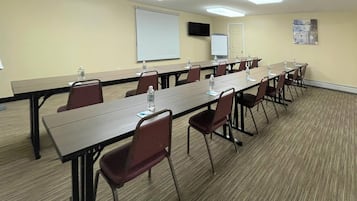 Una sala de conferencias con una larga mesa, sillas, una pantalla de proyector y un televisor en la pared.