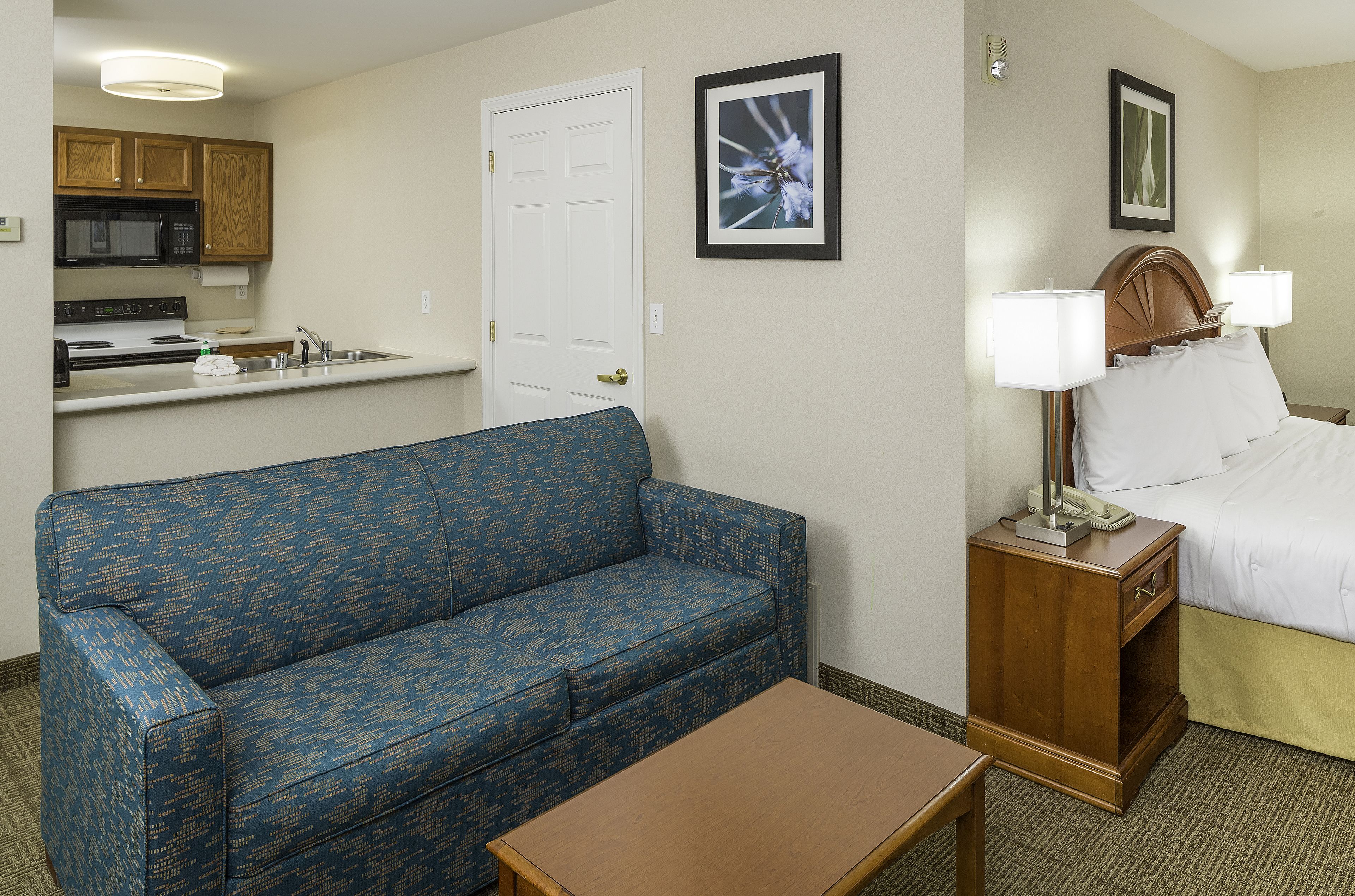 A hotel room with a kitchenette, a bed with two bedside tables, and a blue patterned sofa.
