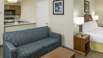 A hotel room with a kitchenette, a bed with two bedside tables, and a blue patterned sofa.