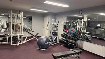 A gym with exercise equipment, a bench, and a rack of dumbbells.