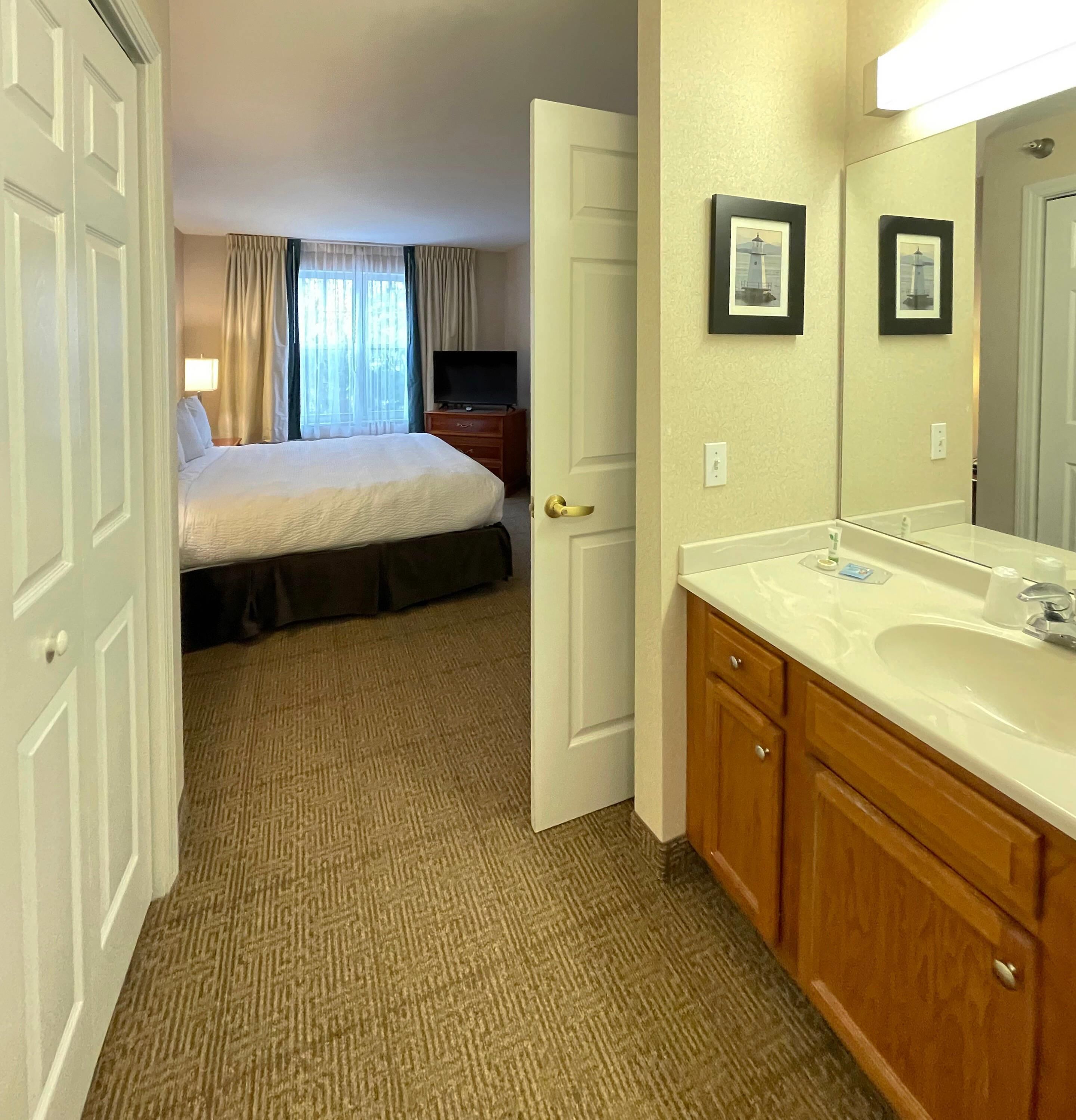 A hotel room with a bed, a television, a bathroom with a sink and mirror, and a door leading to another room.