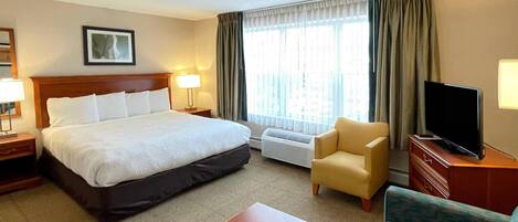 Una habitación de hotel con una cama grande, televisor, sillón, sofá y ventana con cortinas.