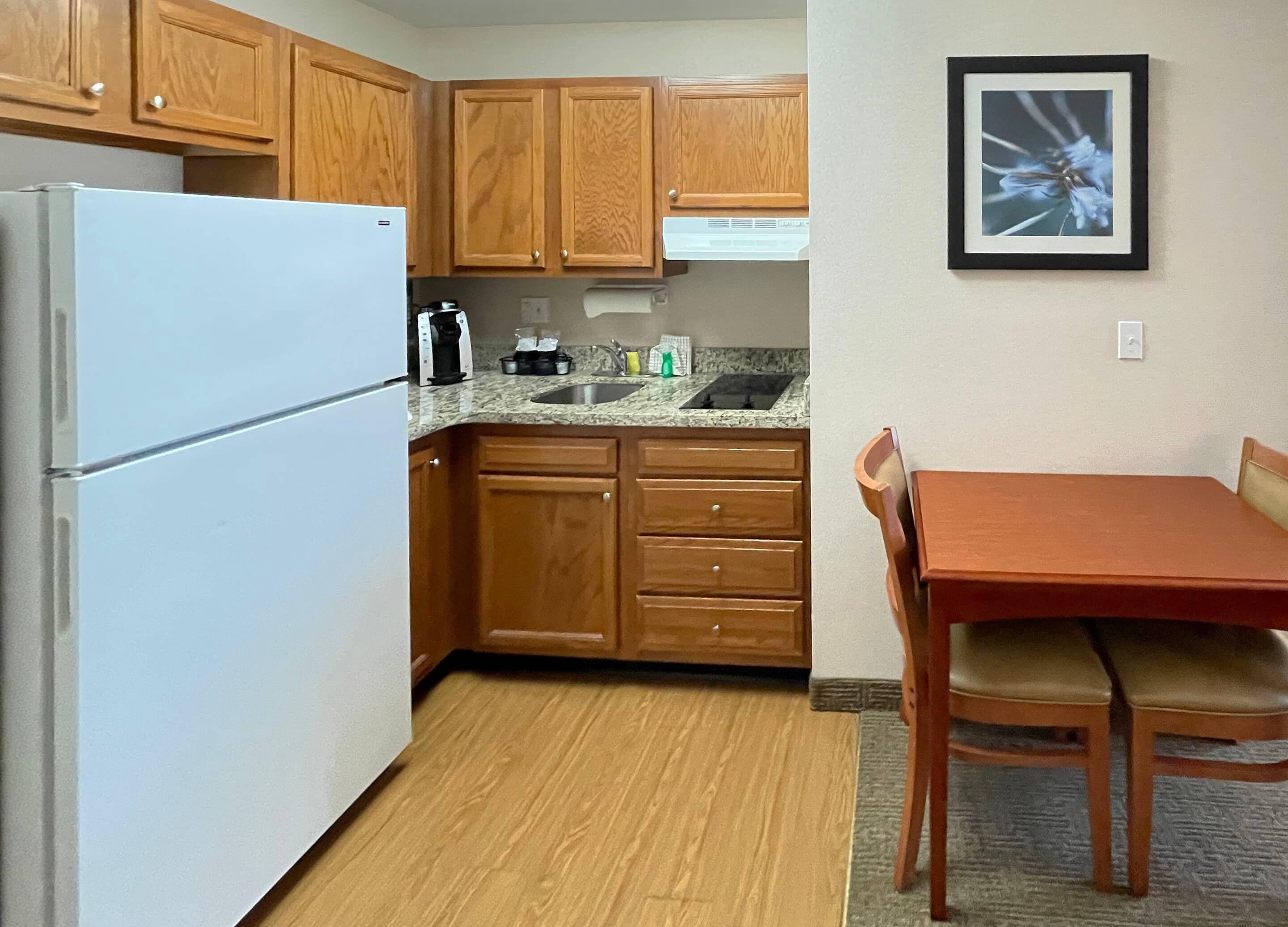 Una cocina con armarios de madera, un refrigerador blanco, una encimera con cafetera y una mesa de comedor con sillas.