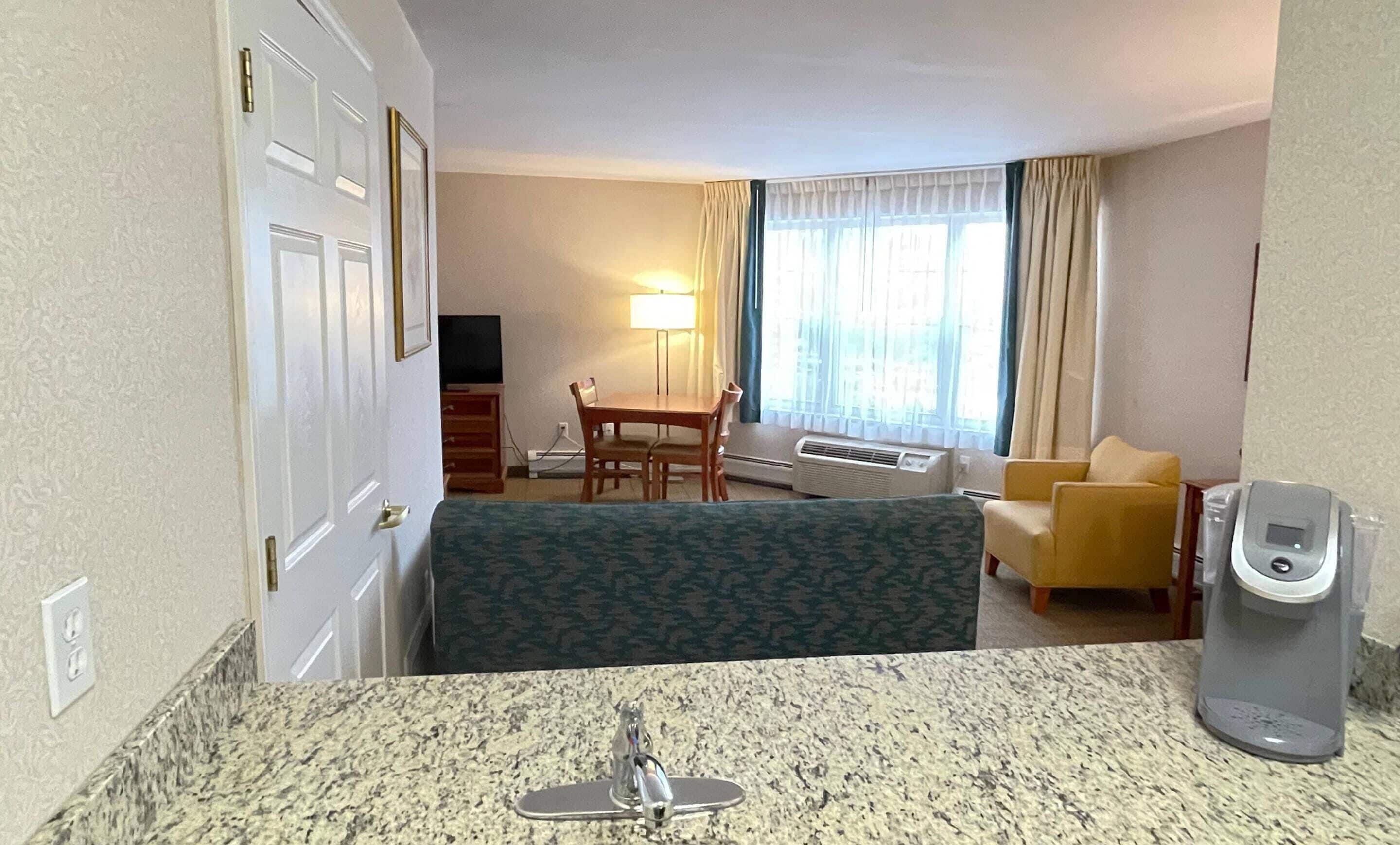 A hotel room with a bed, a small dining table, a sofa, a TV, and a window with curtains.