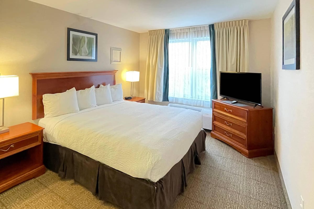 A hotel room with a large bed, bedside tables, a TV, and a window with curtains.