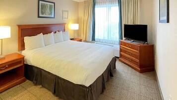 A hotel room with a large bed, bedside tables, a TV, and a window with curtains.