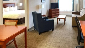 Ein Hotelzimmer mit Bett, Schreibtisch, Sessel, Sofa, Fernseher und Kommode.
