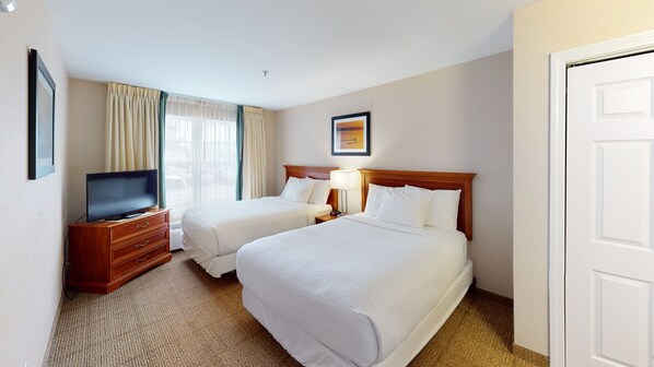 A hotel room with two beds, a TV, a desk, and a window with curtains.