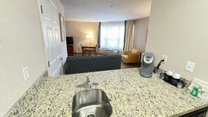 Ein Hotelzimmer mit einer Granit-Arbeitsplatte, einem Edelstahl-Spülbecken, einer Mikrowelle, einer Kaffeemaschine und einem kleinen Tisch mit einem Stuhl.