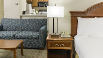A hotel room with a blue patterned sofa, a wooden nightstand with a lamp, a telephone, and a bed with white linens.
