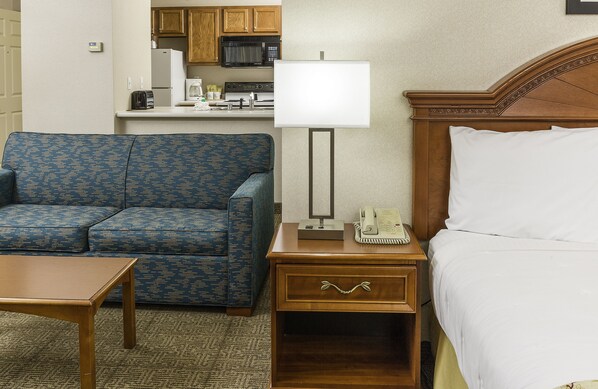 A hotel room with a blue patterned sofa, a wooden nightstand with a lamp, a telephone, and a bed with white linens.