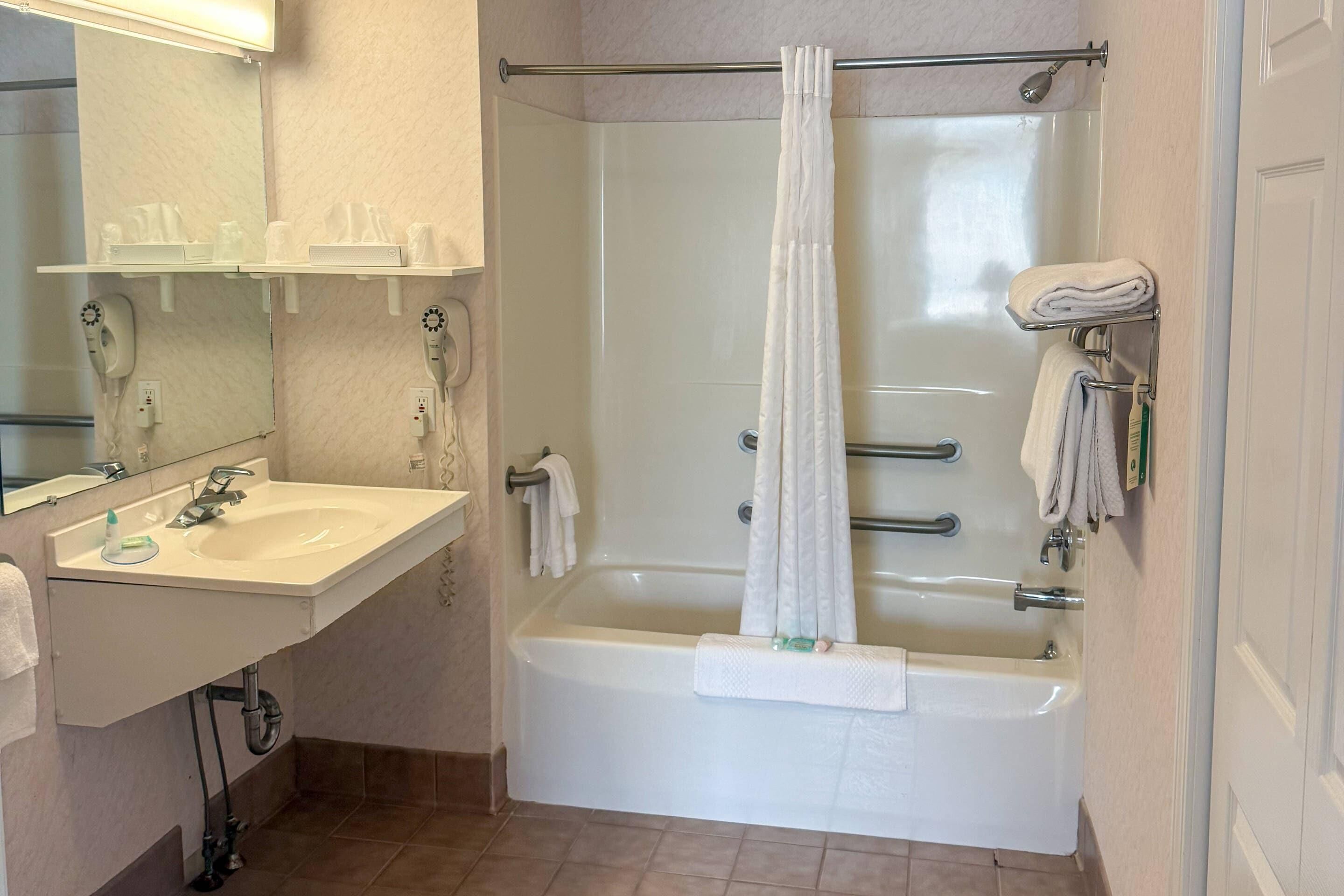 A bathroom with a bathtub, a sink, a mirror, and a towel rack.