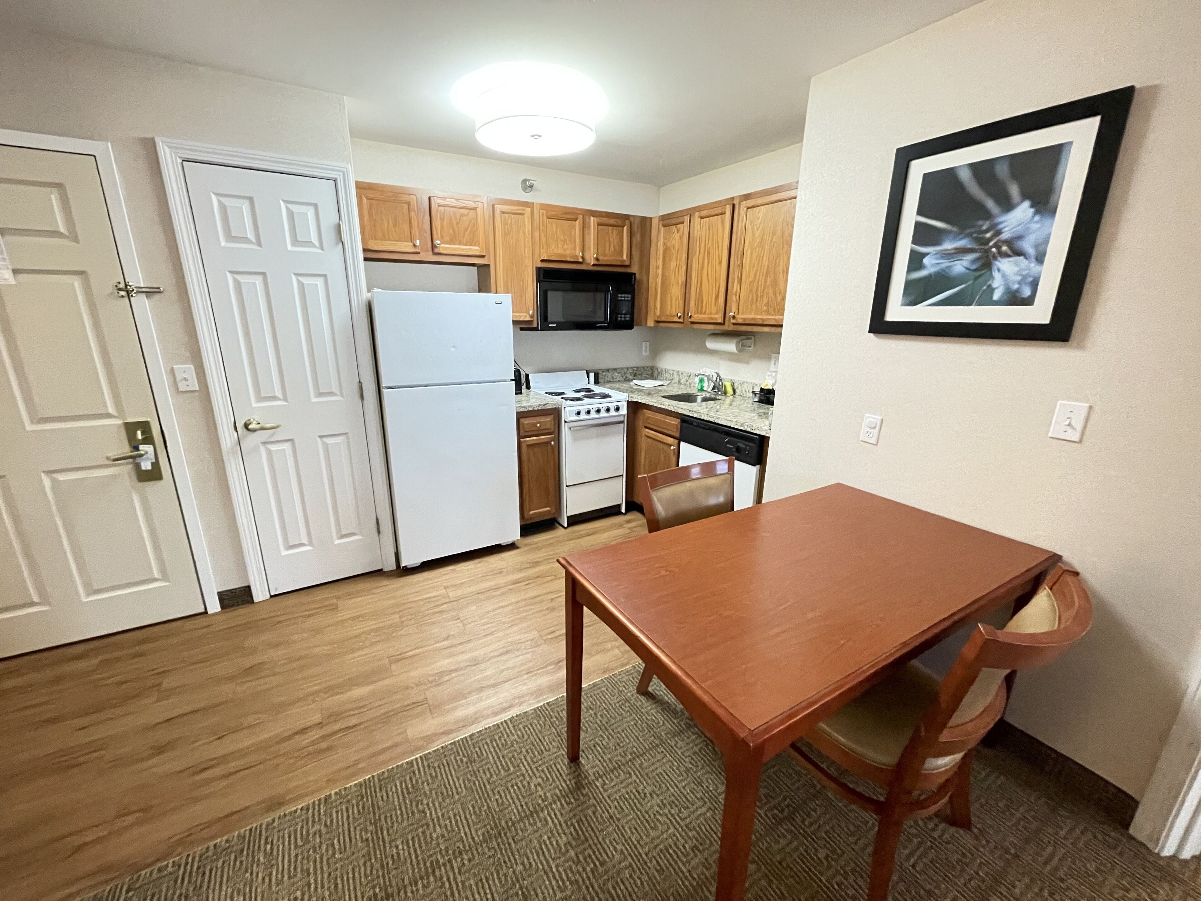 A compact kitchen with wooden cabinets, a white refrigerator, a stove, and a microwave. There is a dining table with chairs.