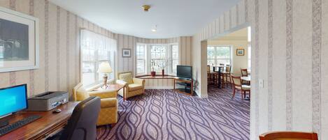 Habitación de hotel con escritorio, computadora, sillas, televisor y comedor con mesa y sillas.