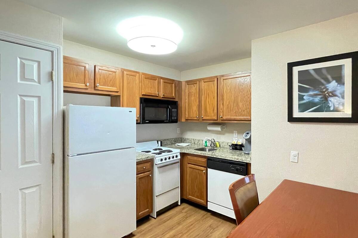 A compact kitchen with wooden cabinets, a white refrigerator, a stove, a microwave, and a dishwasher.