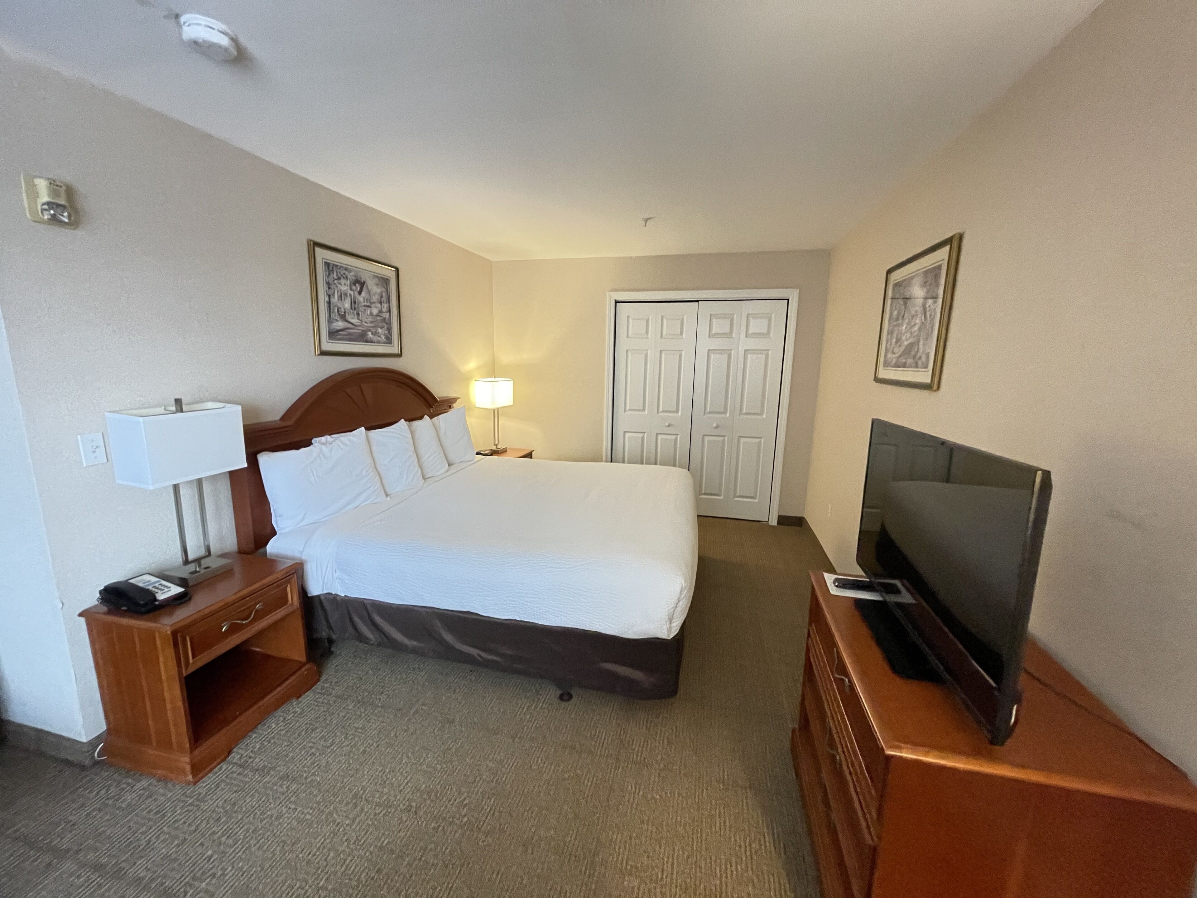 Habitación de hotel con cama, lámpara de noche, televisión, mesita de noche de madera y una puerta con cerradura.
