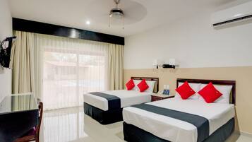 A hotel room with two beds, a desk, a chair, a ceiling fan, and an air conditioning unit.