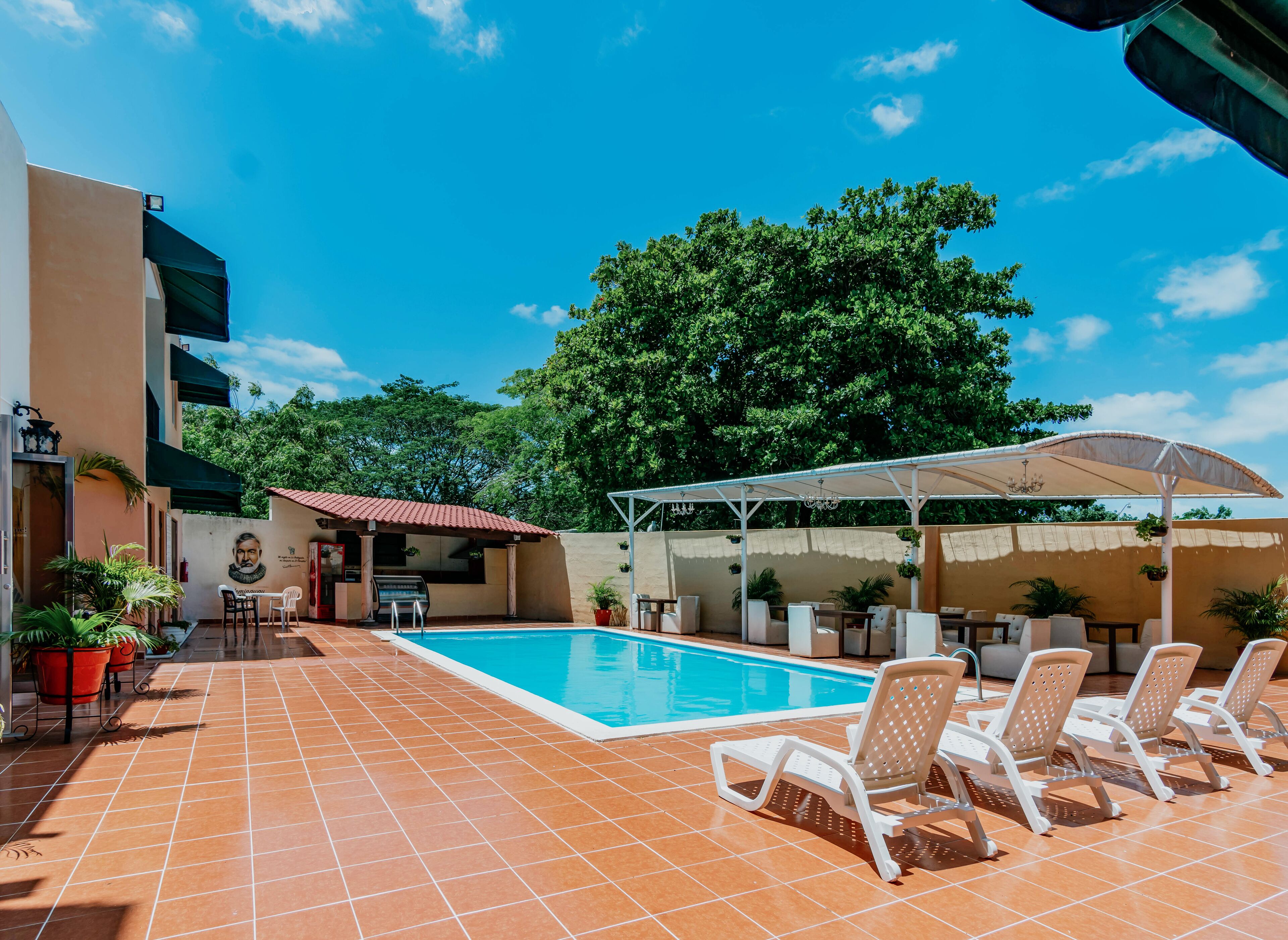 A swimming pool with lounge chairs, a covered seating area, and a mural on the wall.