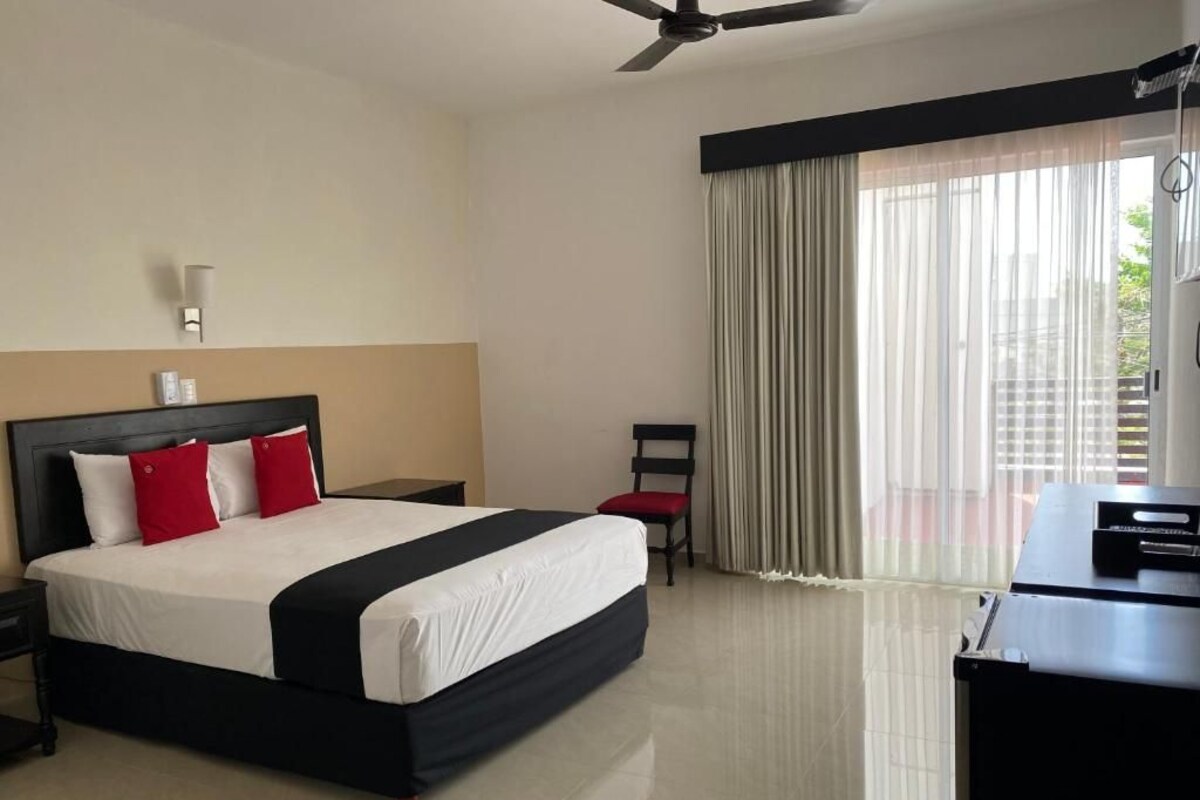 Ein Hotelzimmer mit einem großen Bett, einem Schreibtisch, einem Sessel, einem Deckenventilator und einem Fenster mit Vorhängen.
