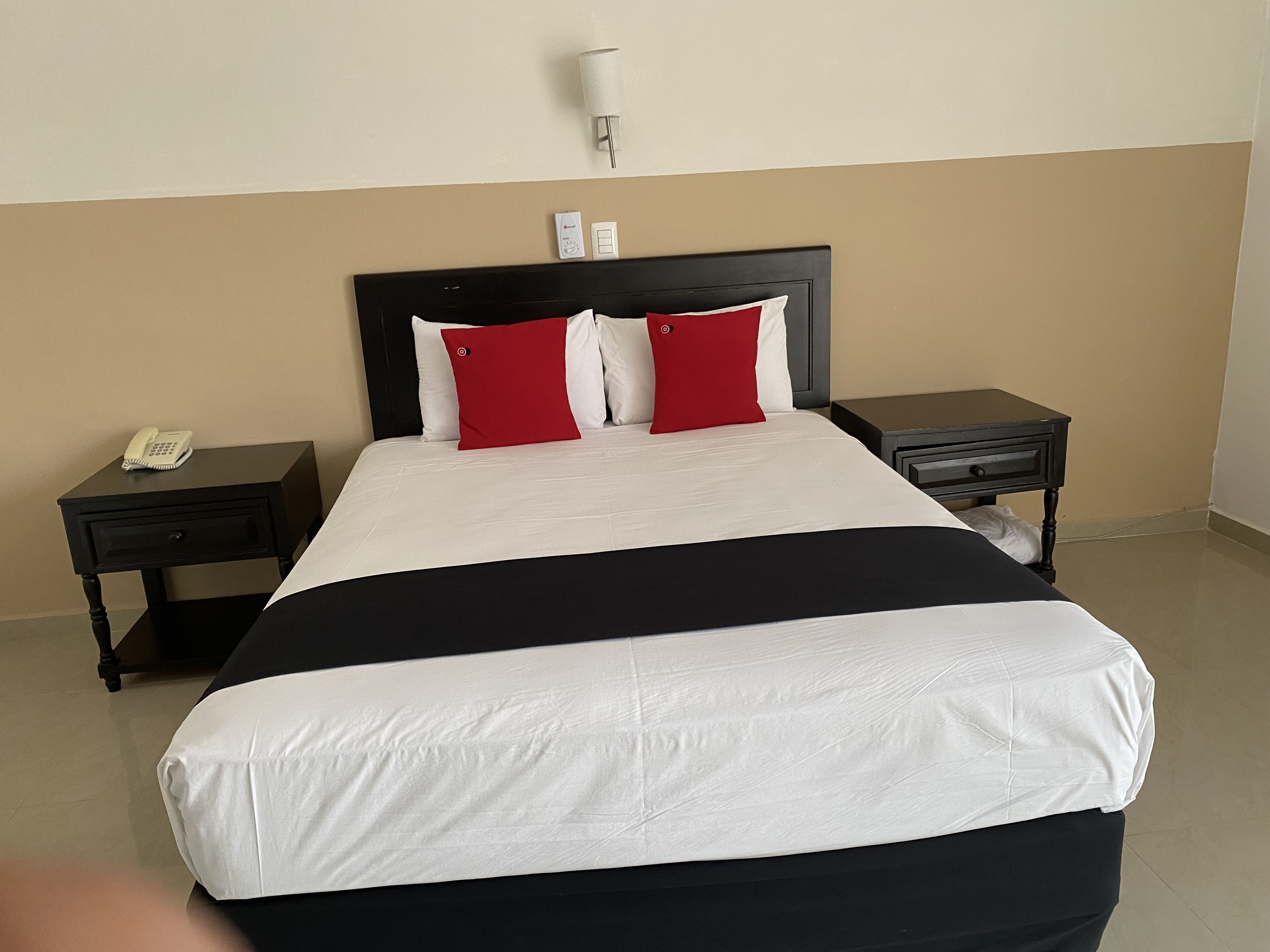 Une chambre d’hôtel avec un grand lit, deux tables de chevet, un téléphone sur l’une des tables et une lampe fixée au mur.