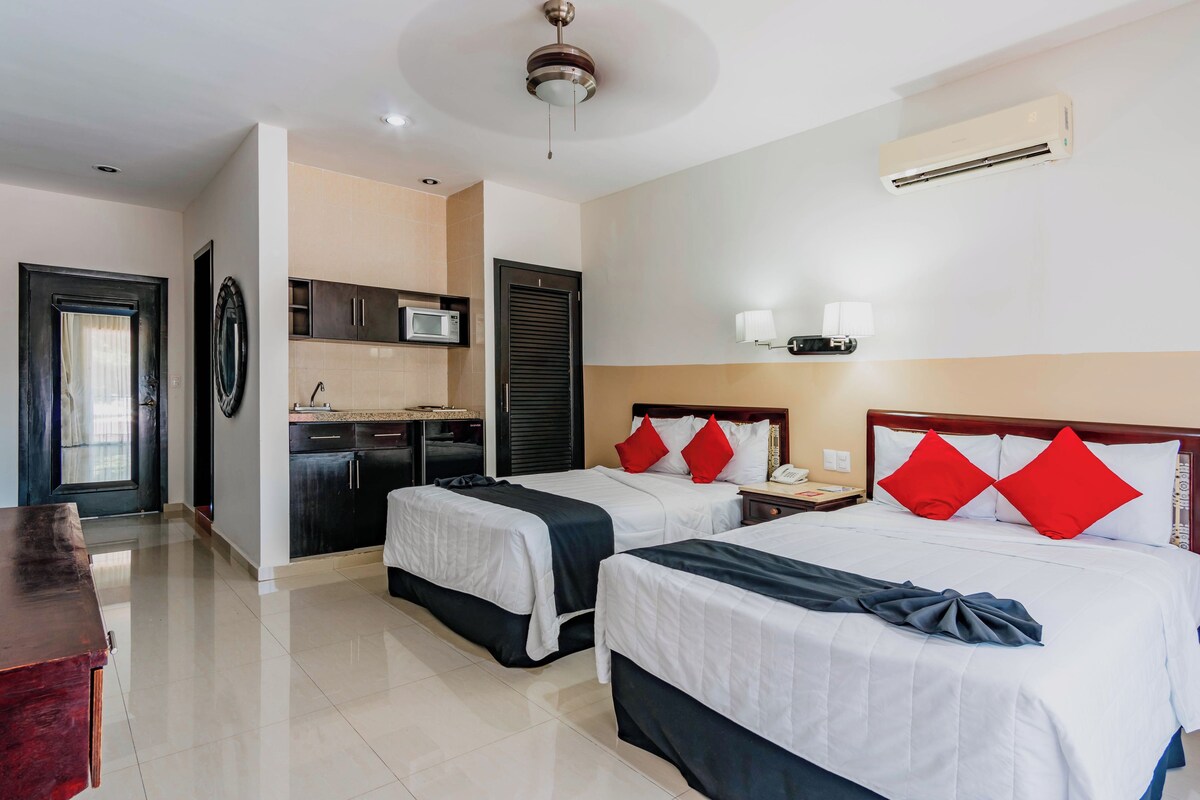 Ein Hotelzimmer mit zwei Betten, einer Küchenzeile, einem Deckenventilator und einer Klimaanlage.