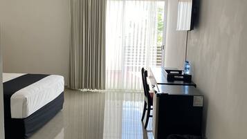Habitación de hotel con cama, escritorio, silla, cubo de basura, ventilador de techo y unidad de aire acondicionado.