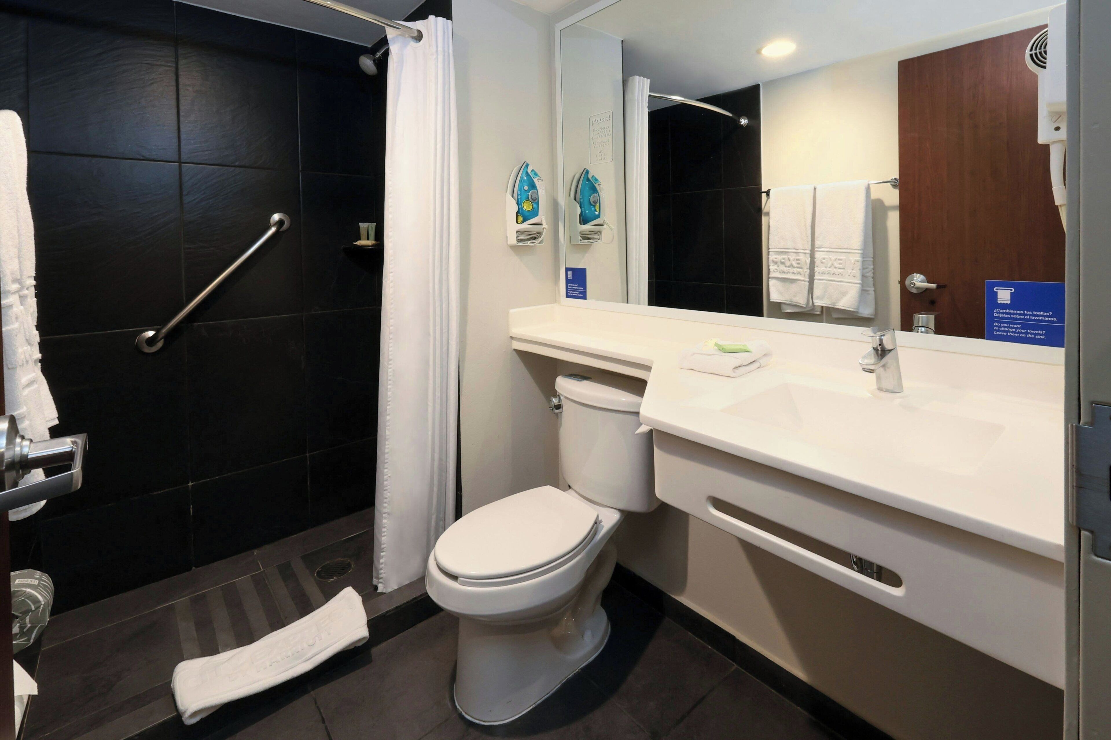 A bathroom with a white toilet, a sink, a shower with a grab bar, and a towel rack.