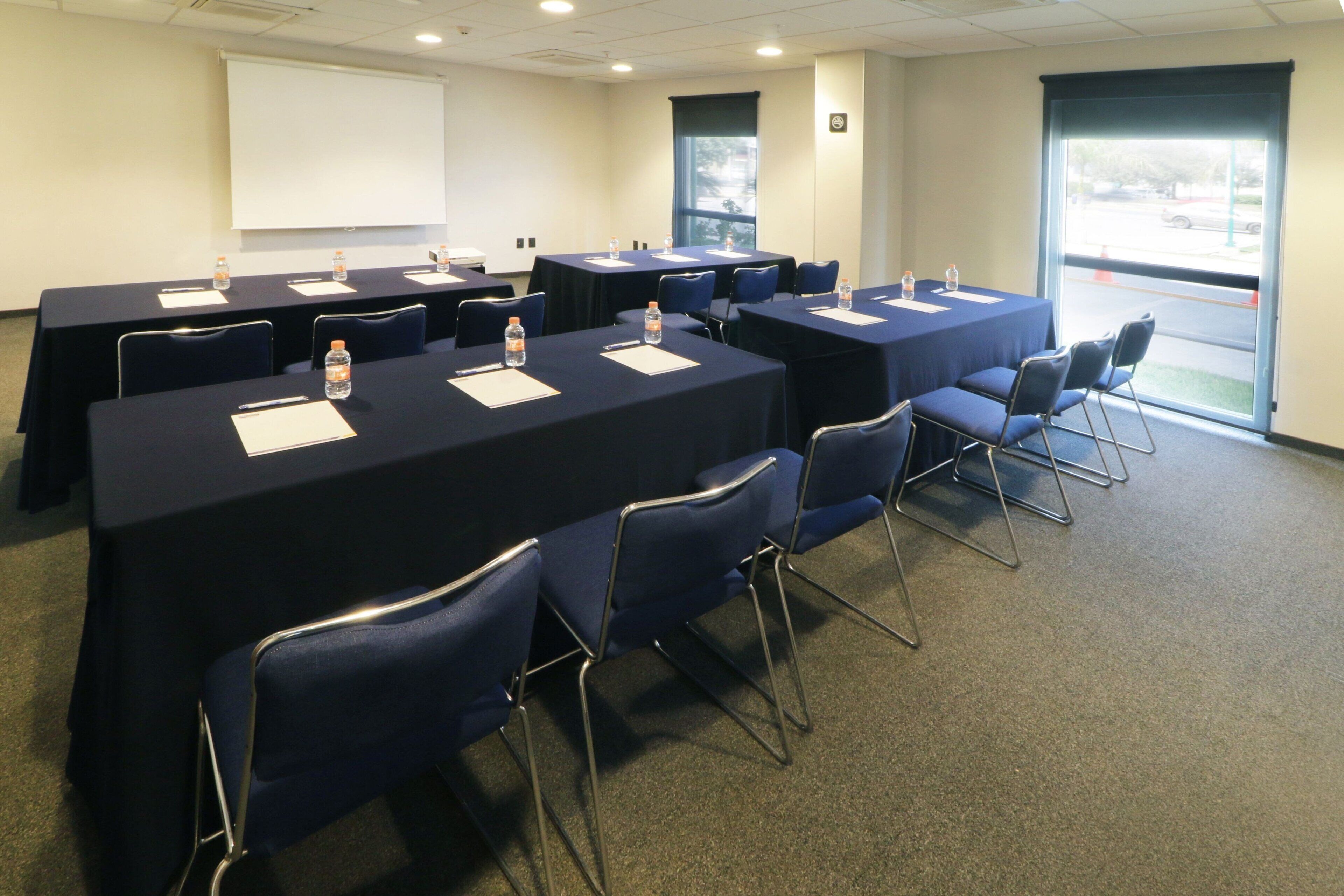 A conference room with multiple tables and chairs, equipped with water bottles and notepads.