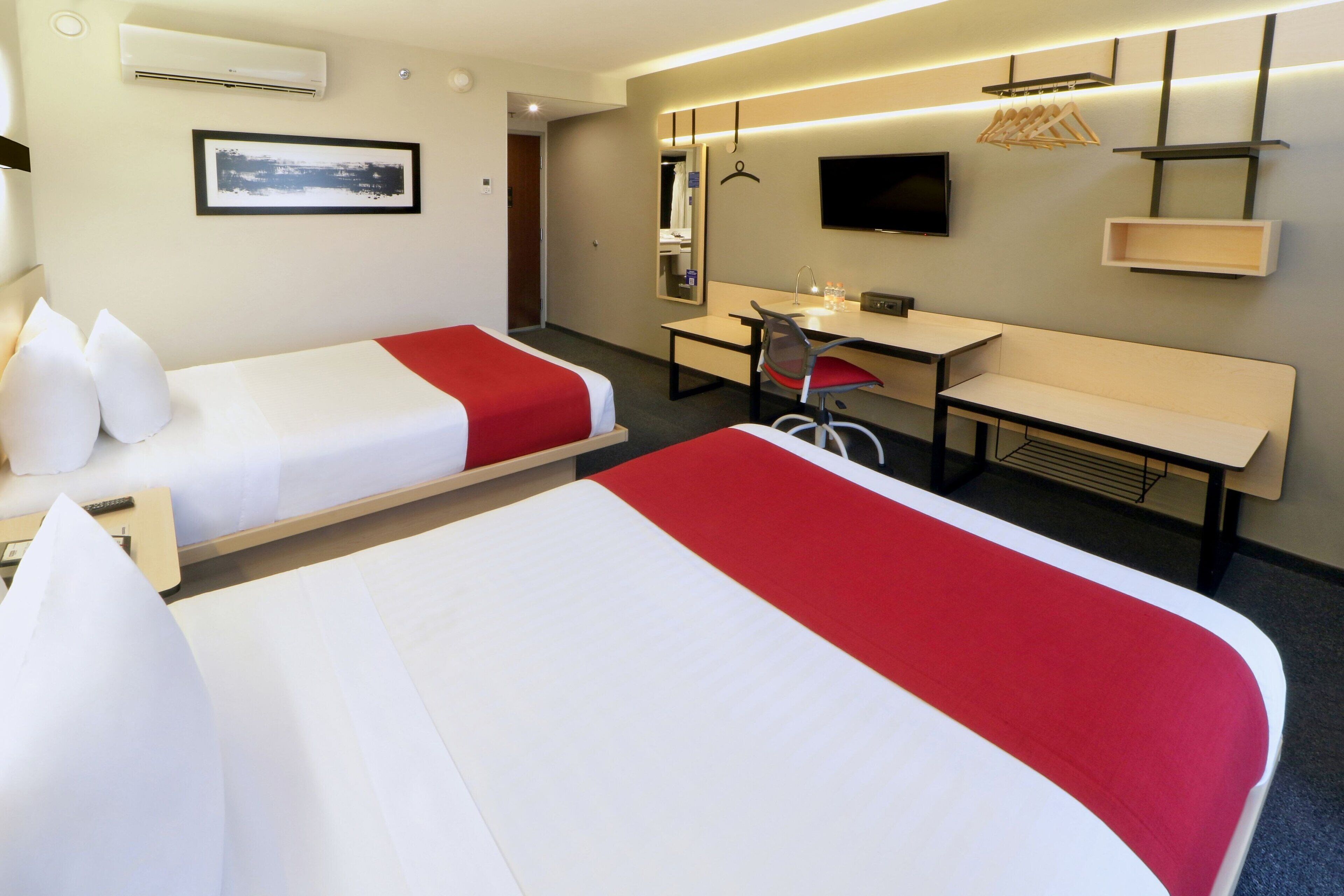 A hotel room with two beds, a desk, a chair, a TV, and a mirror.