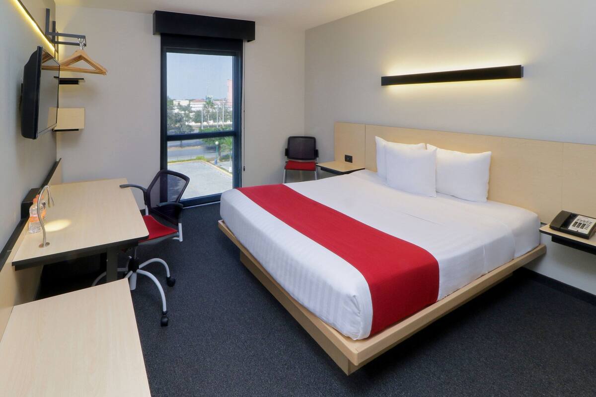 A hotel room with a bed, a desk, a chair, a TV, and a window with a view.
