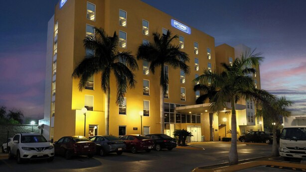 Um hotel com fachada amarela, várias janelas e estacionamento com diversos carros.