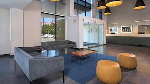 Um hall moderno com um sofá cinzento, mesa de centro de madeira e dois pufes redondos.