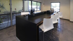 Um espaço de escritório moderno com uma grande mesa preta, cadeiras brancas e amplas janelas que oferecem vistas para o exterior.