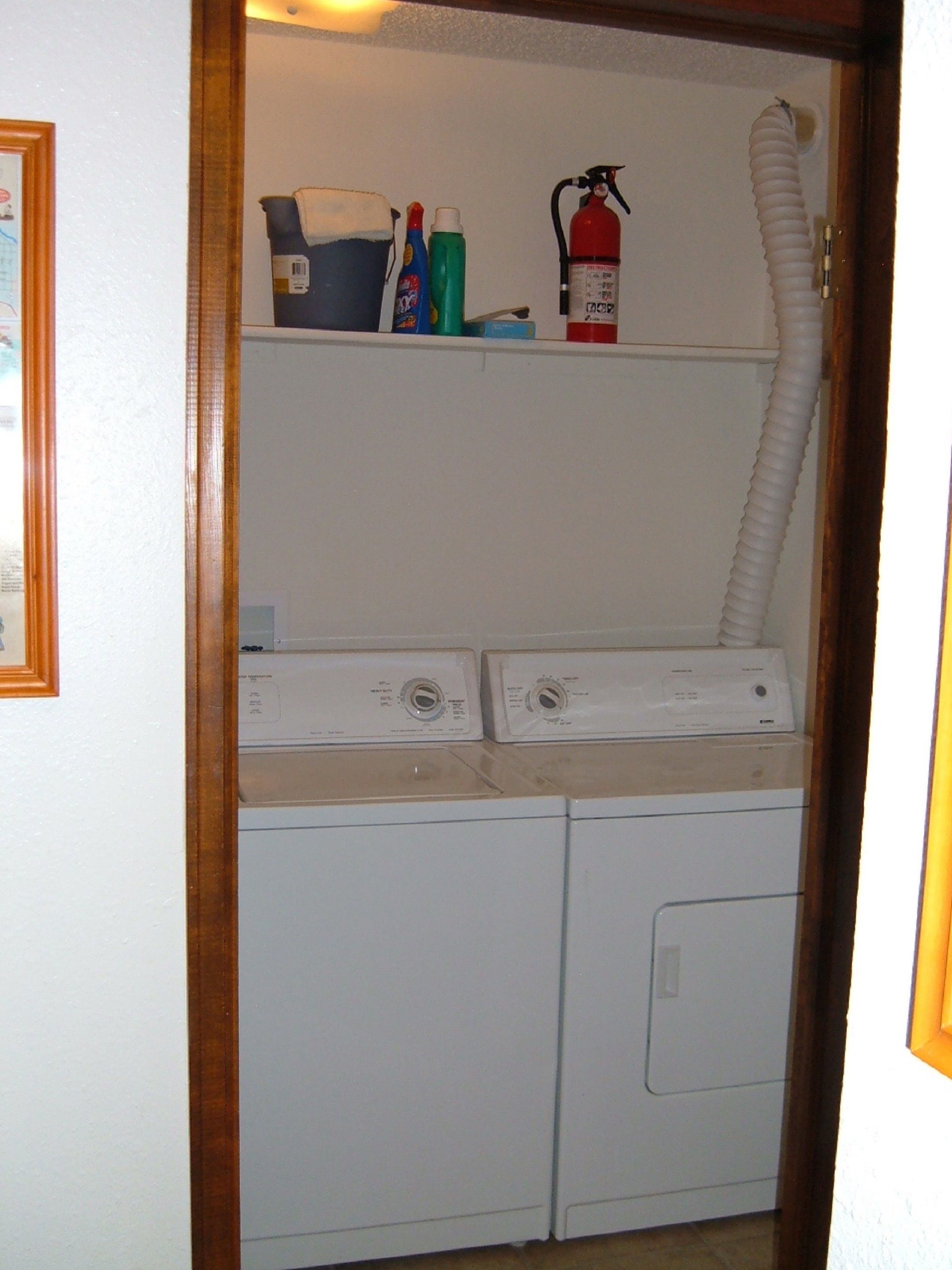 A laundry area with two washing machines, a fire extinguisher, and cleaning supplies on a shelf.