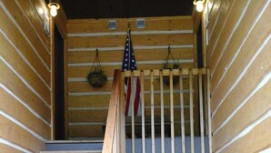 Una escalera de madera con barandilla, un cartel que dice 'WATCHING OVER US', y banderas estadounidenses colgadas del techo.