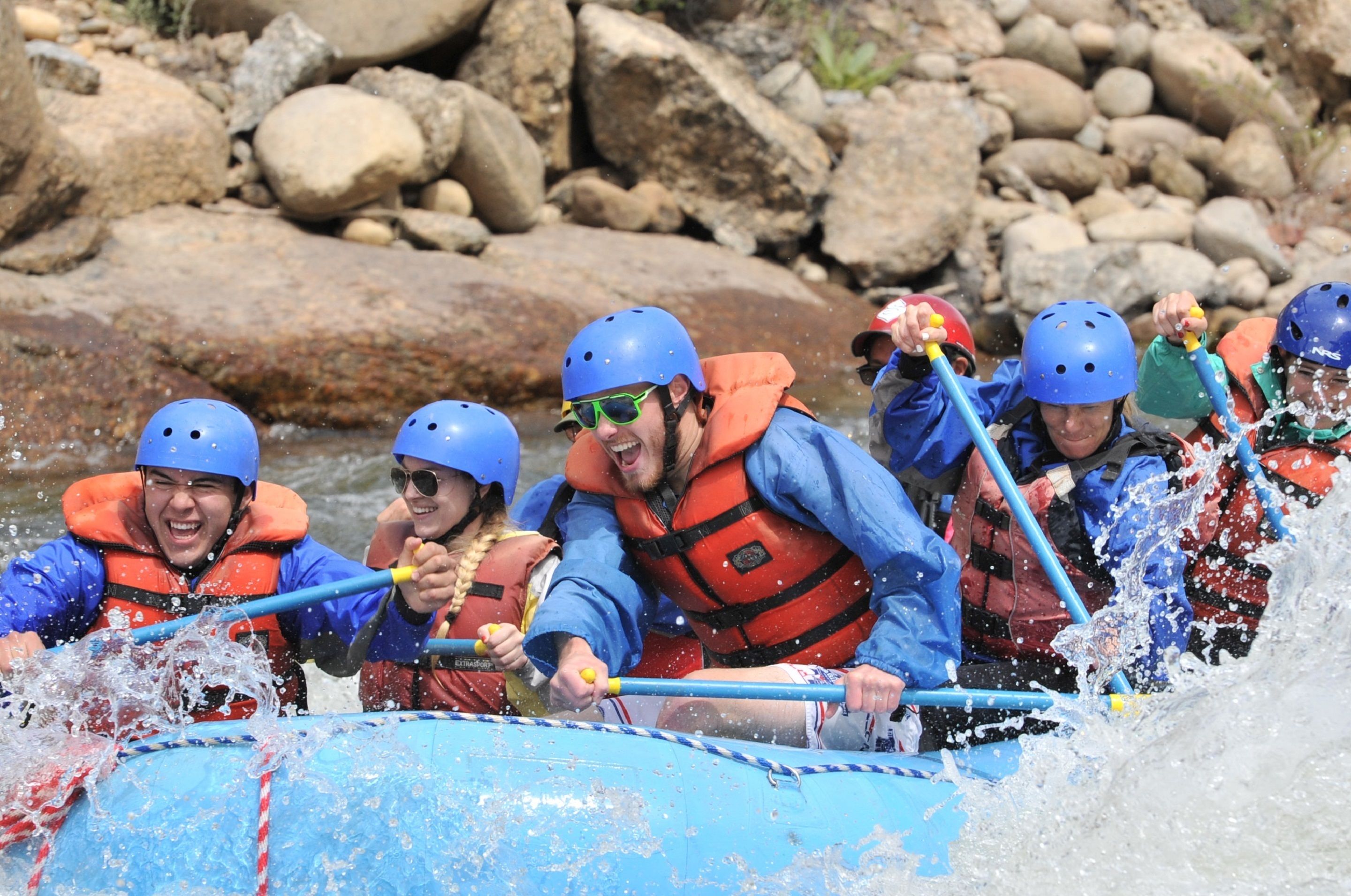 A group of people in a blue raft navigating a river.
