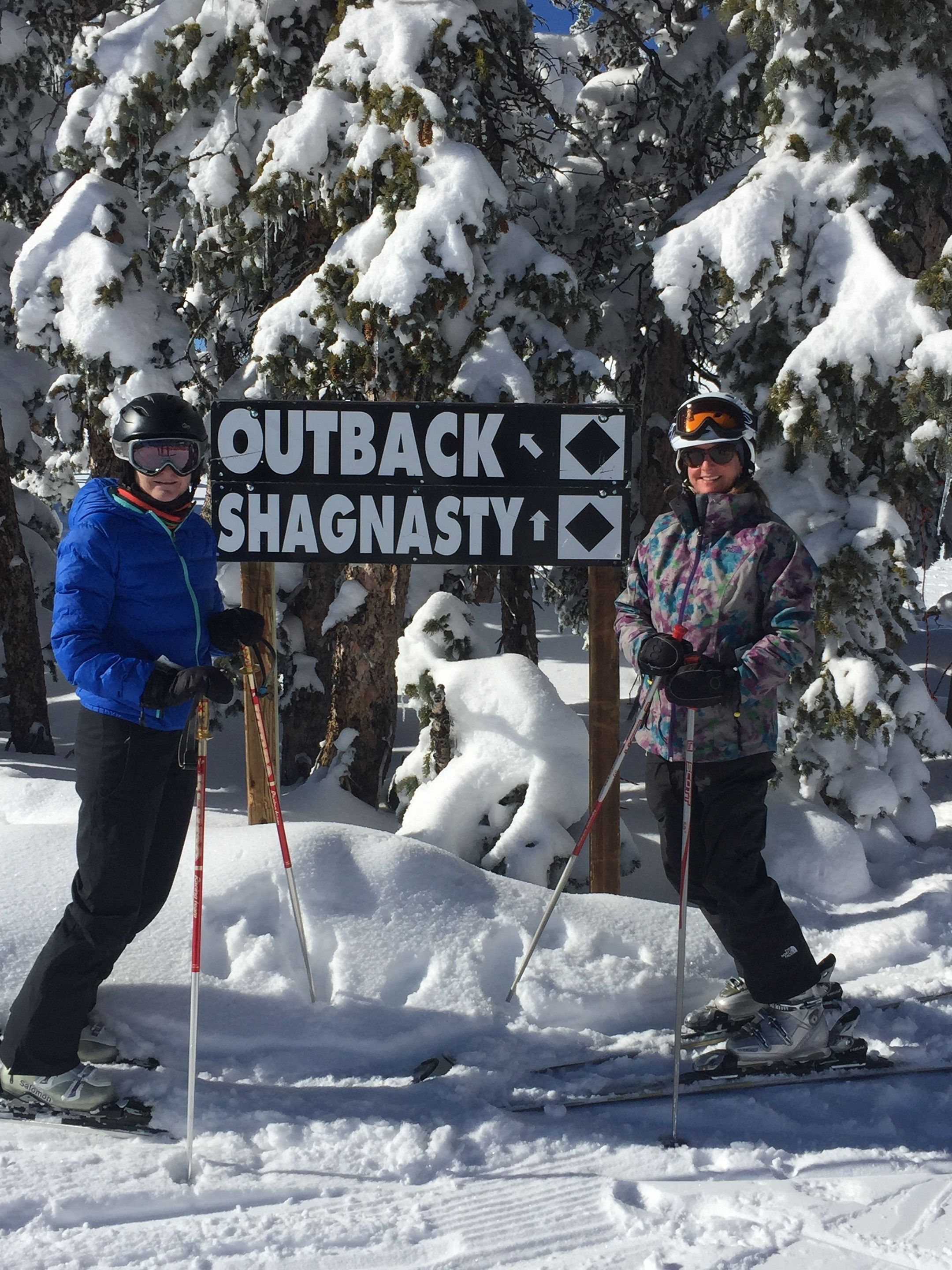 Two skiers standing next to a sign with directions.
