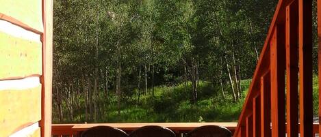 Una terraza de madera con una mesa y sillas, con vistas a una ladera boscosa.