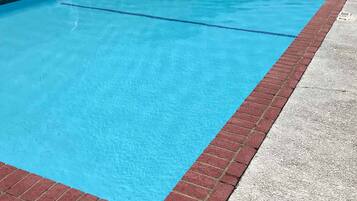 Una piscina rectangular con un borde de ladrillo rojo, rodeada por una terraza con baldosas.