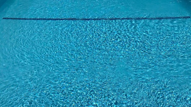 A clear blue swimming pool with visible ripples and a brick border. - Western Motel - Prentiss (Prentiss)