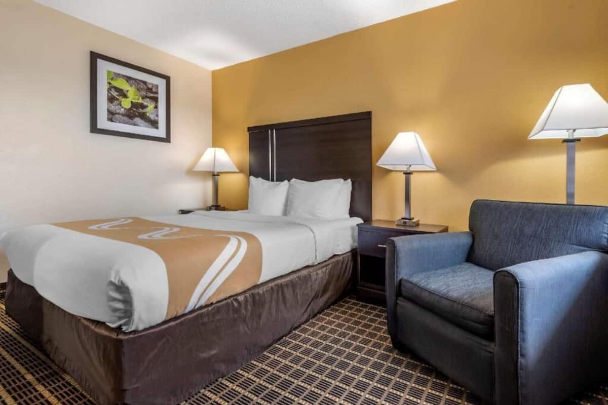 Ein Hotelzimmer mit einem Bett, zwei Nachttischlampen, einem Sessel und einem gemusterten Boden.