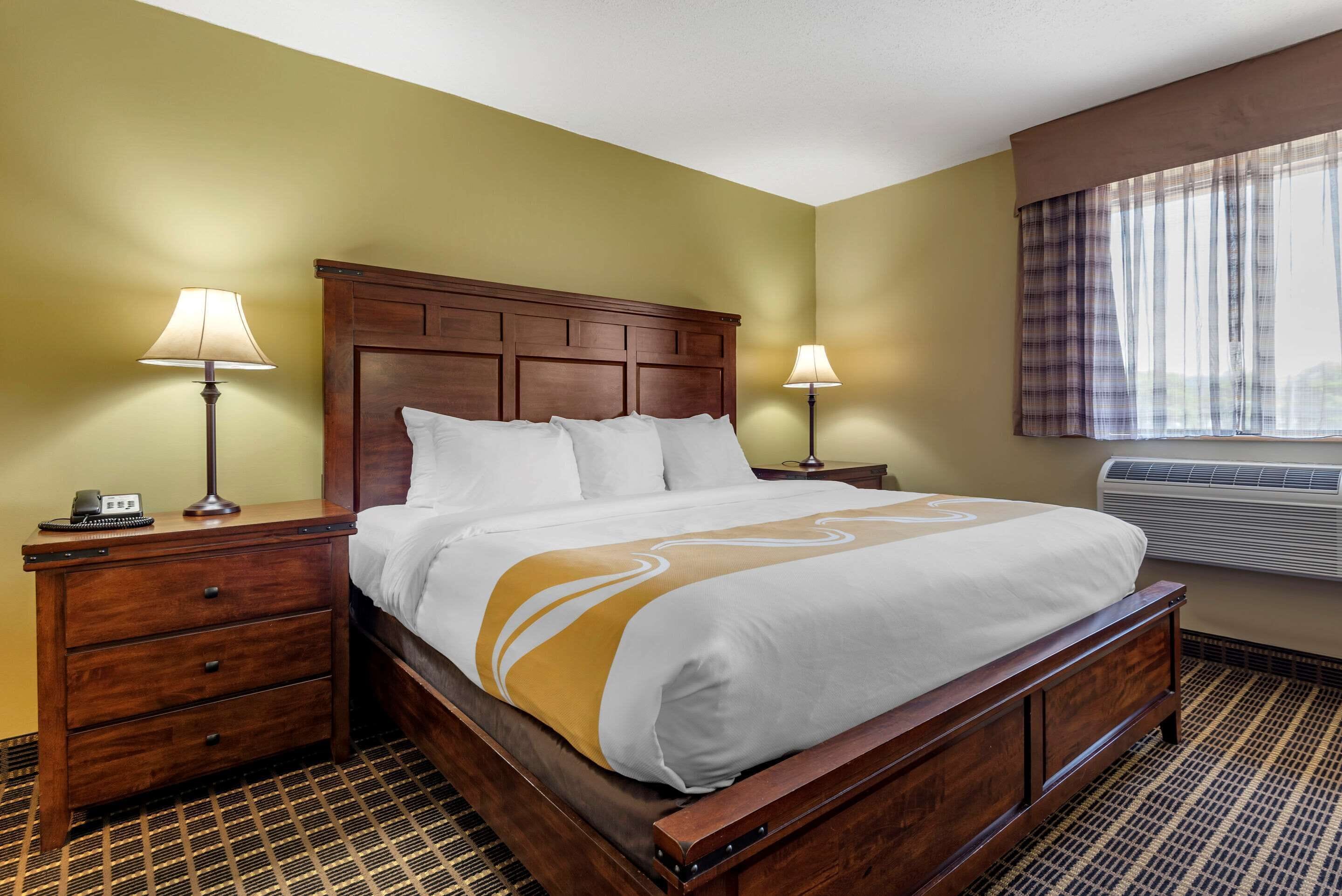 Een hotelkamer met een houten bed, twee nachtkastjes, een vloer met patroon en een raam met gordijnen.