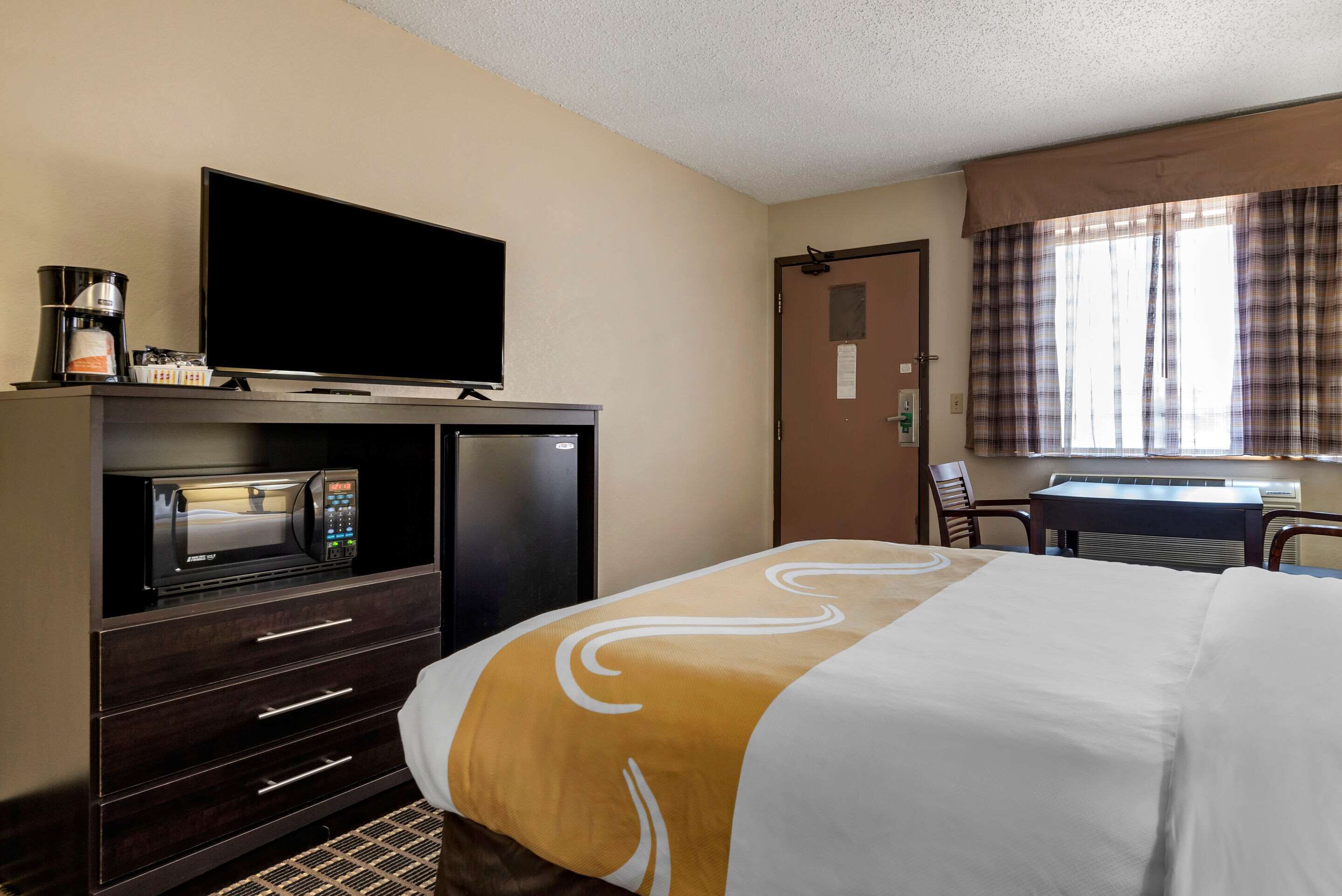 A hotel room with a bed, a TV, a microwave, a coffee maker, and a desk with a chair.