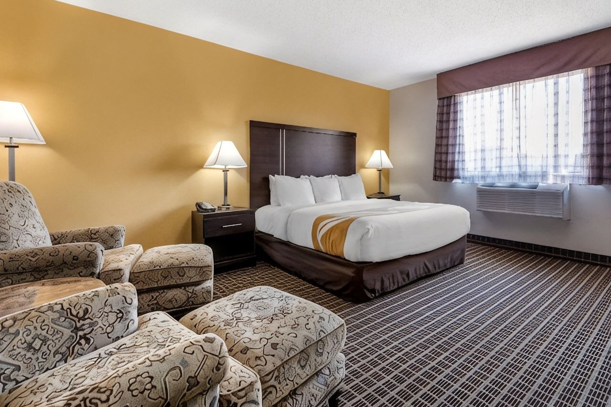 Habitación de hotel con cama, dos mesitas de noche, una silla, un sofá y una ventana con cortinas.