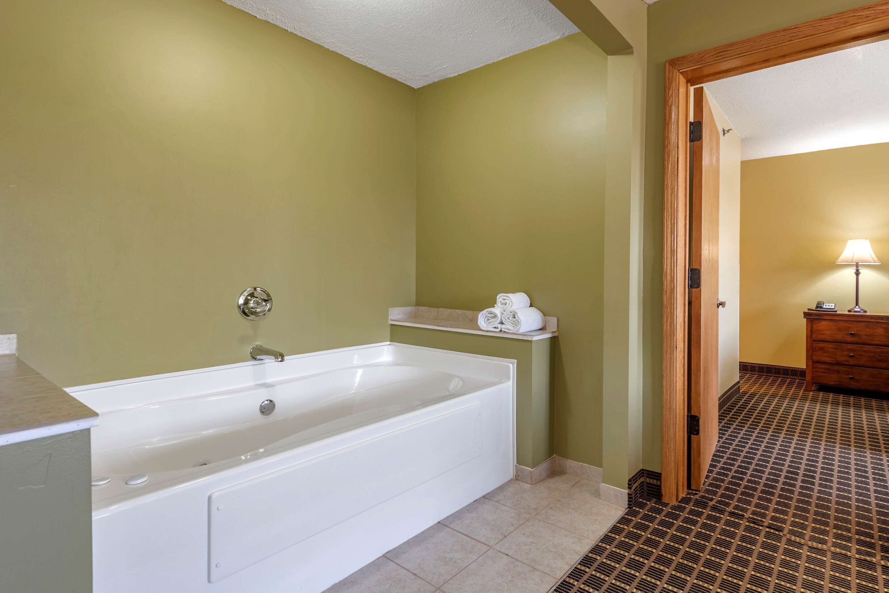 Un baño con una bañera blanca, un perchero para toallas y una puerta de madera que da a otra habitación.