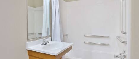 Un baño moderno con lavamanos, espejo y bañera blancos.